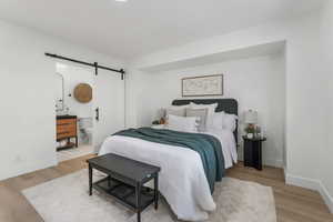 Bedroom with a barn door, wood finished floors, and baseboards