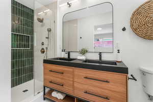 Bathroom featuring toilet, a tile shower, and double vanity