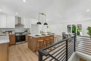 Kitchen with gas stove, wall chimney exhaust hood, light countertops, recessed lighting, and light wood-style flooring