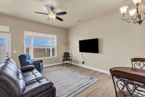 Living area with light wood finished floors, a chandelier, a ceiling fan, and baseboards