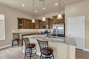 Kitchen with appliances with stainless steel finishes, open shelves, baseboards, light stone countertops, and a sink