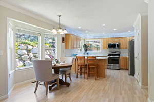 Kitchen featuring appliances with stainless steel finishes, a peninsula, light wood-style flooring, crown molding, and a chandelier