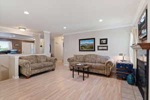 Living area featuring light wood-type flooring, baseboards, crown molding, recessed lighting, and a fireplace with flush hearth