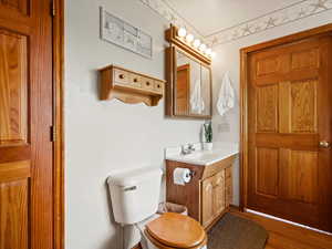 Half bathroom with toilet, vanity, and wood finished floors