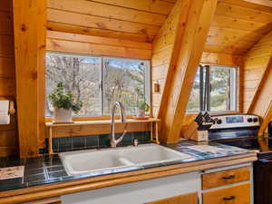 Kitchen with stainless steel range with electric stovetop, vaulted ceiling, a sink, plenty of natural light, and wooden ceiling