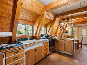 Kitchen featuring stainless steel range with electric stovetop, a sink, tile countertops, wood ceiling, and a kitchen bar