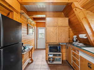 Kitchen featuring freestanding refrigerator, stainless steel microwave, wooden walls, wood ceiling, and beamed ceiling