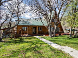 View of front of house with faux log siding, metal roof, and a front lawn