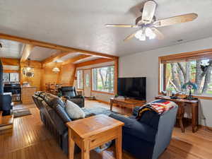 Living area with a wood stove, light wood-style flooring, baseboards, ceiling fan, and a textured ceiling