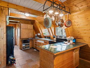 Kitchen featuring tile counters, stainless steel appliances, a sink, wooden walls, and wood ceiling