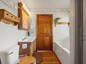 Full bathroom featuring wood finished floors, a bath, vanity, and toilet