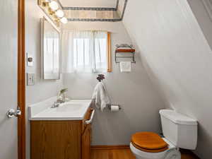 Bathroom with toilet, vanity, wood finished floors, and baseboards