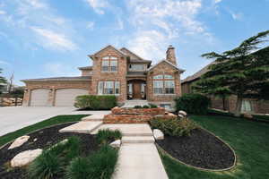 View of front of house featuring a front lawn, driveway, a garage, a chimney, and stone siding