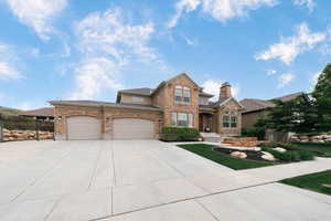 View of front of house with driveway, fence, an attached garage, a chimney, and stone siding