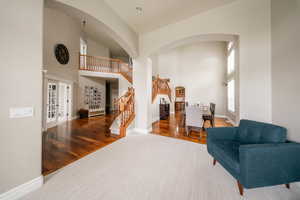 Living area featuring a towering ceiling, arched walkways, stairway, baseboards, and wood finished floors