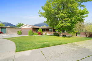Ranch-style house featuring driveway, a front yard, an attached garage, and a mountain view