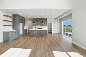 Kitchen with open shelves, light wood finished floors, light countertops, a center island with sink, and recessed lighting