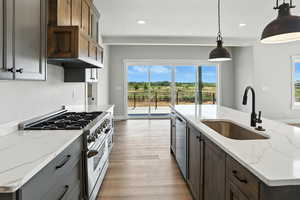 Kitchen featuring appliances with stainless steel finishes, light wood-style flooring, recessed lighting, hanging light fixtures, and light stone countertops