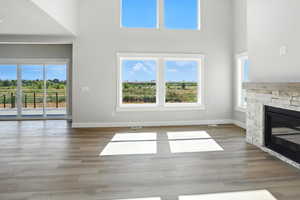 Unfurnished living room featuring a towering ceiling, healthy amount of natural light, a fireplace, and wood finished floors