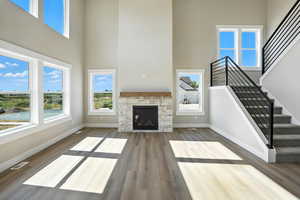 Unfurnished living room featuring a towering ceiling, wood finished floors, stairs, and a stone fireplace