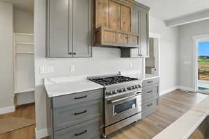 Kitchen featuring high end stove, gray cabinets, light wood-type flooring, custom exhaust hood, and light stone countertops