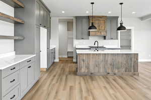 Kitchen with open shelves, light wood-style flooring, recessed lighting, gray cabinets, and a center island with sink