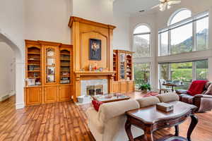 Living area featuring a towering ceiling, a premium fireplace, arched walkways, ceiling fan, and hardwood / wood-style flooring