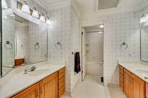 Bathroom featuring wallpapered walls, ornamental molding, two vanities, baseboards, and a bath