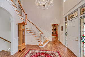 Foyer with a towering ceiling, wood finished floors, arched walkways, a decorative wall, and a chandelier