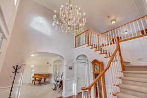 Staircase with arched walkways, a towering ceiling, a chandelier, ornamental molding, and baseboards