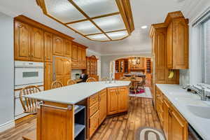 Kitchen featuring white oven, a kitchen island with sink, arched walkways, wood-type flooring, and light countertops
