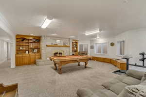 Game room featuring light colored carpet, a brick fireplace, crown molding, built in shelves, and a textured ceiling