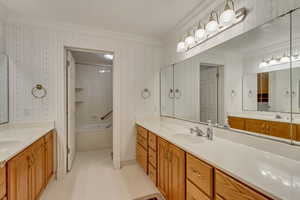 Bathroom with wallpapered walls, crown molding, two vanities, and shower / tub combination