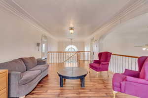 Living area with arched walkways, ornamental molding, wood finished floors, a chandelier, and ceiling fan