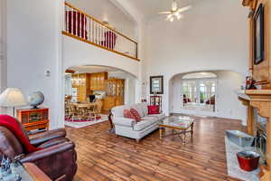 Living room with arched walkways, ceiling fan, ornamental molding, hardwood / wood-style floors, and a towering ceiling
