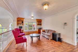 Living area featuring ornamental molding, arched walkways, wood finished floors, and baseboards