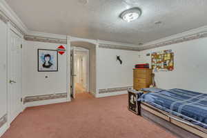 Bedroom with a textured ceiling, light colored carpet, ornamental molding, arched walkways, and baseboards