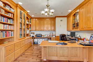Office space with built in desk, light wood-type flooring, recessed lighting, and a chandelier