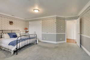 Carpeted bedroom with wallpapered walls and ornamental molding