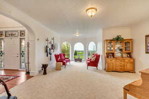 Living area with arched walkways, carpet floors, crown molding, a textured ceiling, and baseboards