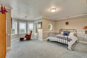 Carpeted bedroom featuring wallpapered walls, a textured ceiling, crown molding, and baseboards