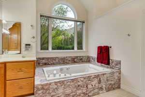 Bathroom featuring a jetted tub, lofted ceiling, and vanity