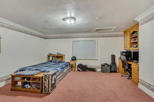 Bedroom featuring an office area, a textured ceiling, attic access, carpet floors, and ornamental molding
