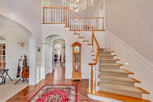 Entrance foyer with a decorative wall, arched walkways, wood finished floors, a towering ceiling, and a chandelier