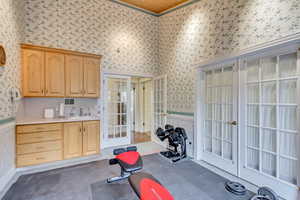 Workout area with wallpapered walls, french doors, a sink, and wainscoting