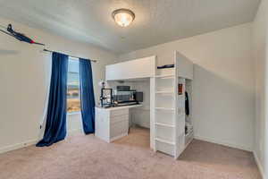 Unfurnished bedroom featuring light colored carpet, a textured ceiling, and baseboards