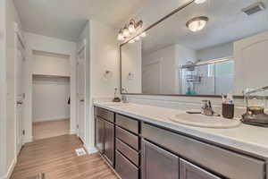 Full bath with a shower stall, double vanity, wood finished floors, and baseboards