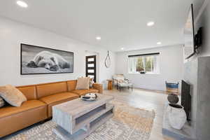 Living room featuring recessed lighting, light wood-style flooring, a fireplace with raised hearth, and baseboards