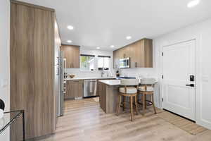 Kitchen with appliances with stainless steel finishes, a sink, a breakfast bar, a peninsula, and brown cabinetry