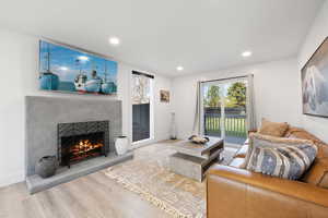 Living room featuring a warm lit fireplace, wood finished floors, recessed lighting, and baseboards